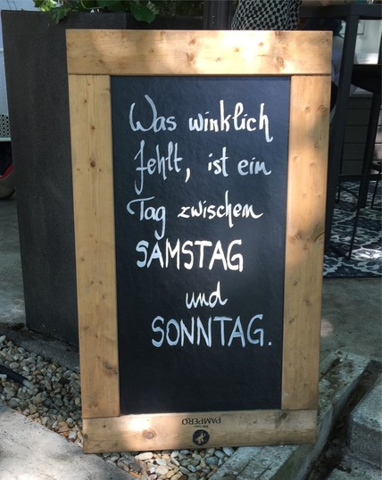 Schild mit Aufschrift „Was wirklich fehlt, ist ein Tag zwischen SAMSTAG und SONNTAG.“