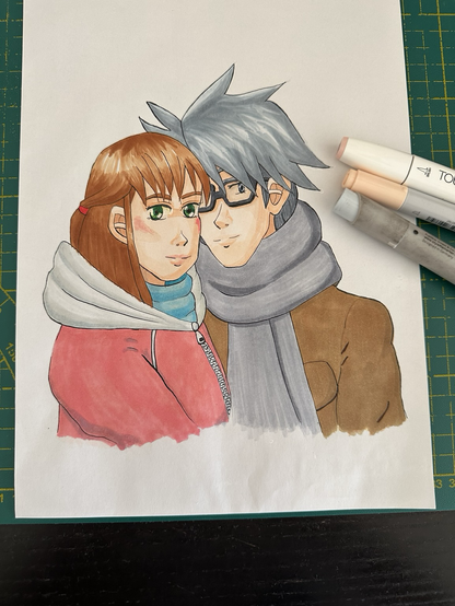 Photo of an alcohol marker drawing of a girl and a boy in winter clothing leaning on each other and smiling at the viewer. The drawing lies on a green mat. Three markers lie on top of the drawing.