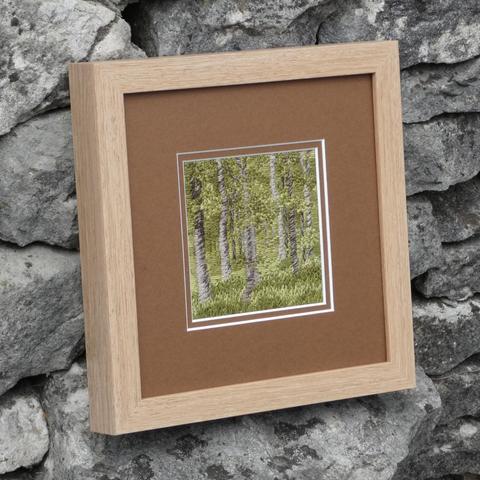 The same artwork, framed in bare wood frame, against a stine wall. Viewed from the othe angle and further away