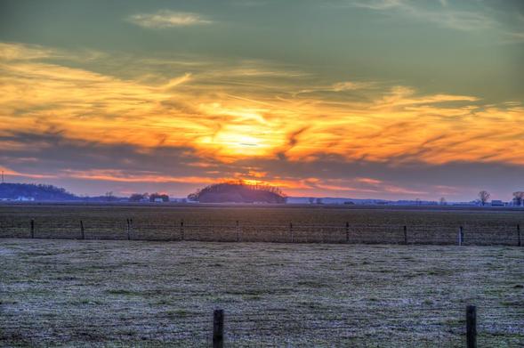 Lost HIll Under a Dazzling Sky

A brilliant sunset sets the sky ablaze with vibrant hues of orange and yellow, casting a warm glow over a vast, open field.