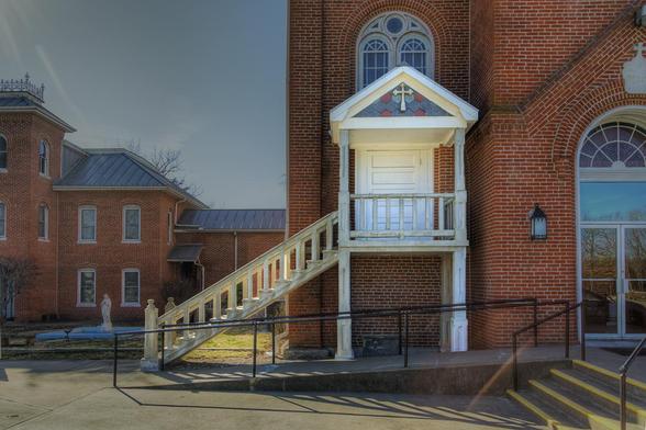 Wooden Staircase on a Church

A red brick church features a distinct white staircase leading to a raised door with a cross design above it.