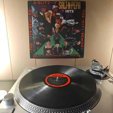 A vinyl record sits on a turntable. Behind the turntable, a vinyl album outer sleeve is displayed. The front cover shows 4 different images of Salt 'N' Pepa as they pose for the camera in each one.