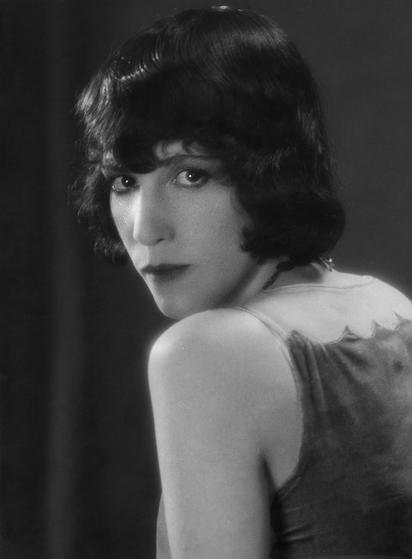 MGM publicity portrait of Lorna Moon (1926)
Academy of Motion Pictures Arts and Sciences / Academy Film Archive

A black-and-white photograph of a dark-haired, dark-eyed young woman, wearing a sleeveless dress which leaves here arms and shoulders bare. Her hair is cut in a 1920s bob. She has her left side turned towards us, and she is looking over her shoulder at the camera.