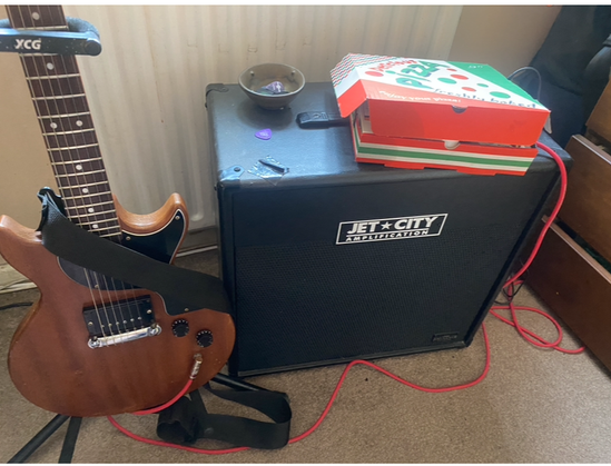 Guitar lead going into a pizza box, containing amp and pedals.