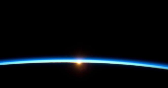 Aufnahme des Sonnenaufgangs aus großer Höhe. Ein heller Streifen schiebt sich über den ründlichen Horizont.
