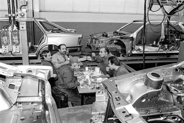 Fünf Arbeiter sitzen in der Montagehalle von Ford bei der Frühstückspause