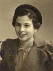 Vintage black and white photo of a smiling girl wearing a beret and a coat with a lapel bow.