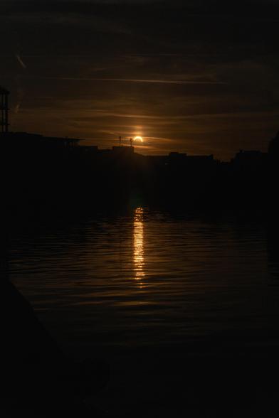 An orange sun reduced to a crescent as the moon entirely blocks out roughly the bottom 80% of it. It hangs ominously just above an angular horizon in a sky lightly pattern by the thinnest of hazy clouds.