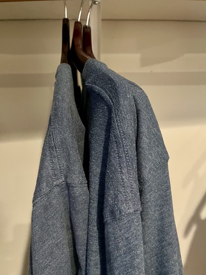 Three identical blue t-shirts on hangers in a hotel room closet