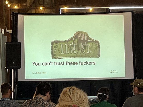 Projected slide of a street sign with “LLM ST.” on the sign and “You can’t trust these fuckers” on the slide