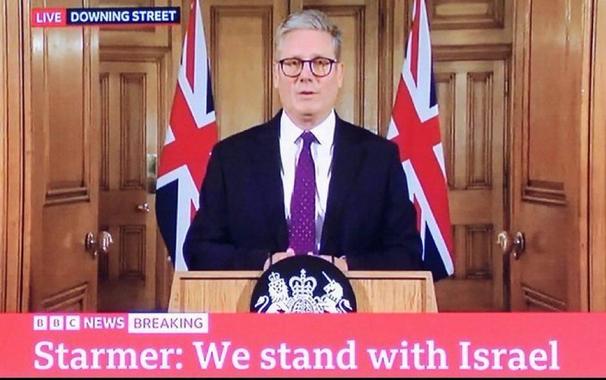 Keir Starmer, stood in front of a UK gov lecturn with the caption “we stand with Israel”