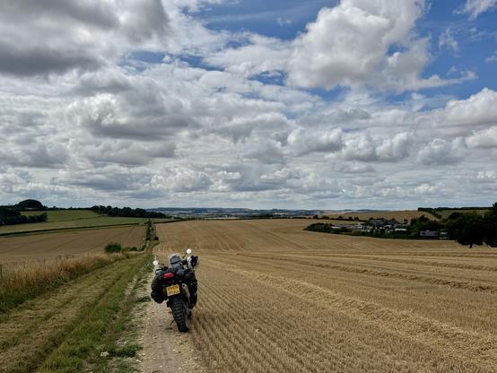 My motorbike on the side of a recently harvested wheat field, looking down over the downs. 
