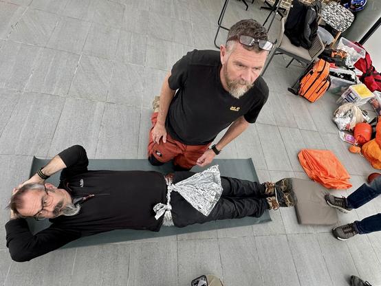 JP knelt next to a patient whilst demonstrating using a silver blanket to apply a pelvis support