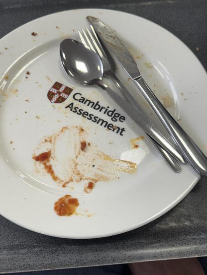 Photo of an empty dinner plate that has the Cambridge Assessment logo on it. Cutlery on the plate, and some ketchup. 