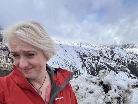 Selfie of me in a GoreTex waterproof with mountains behind covered in snow. 