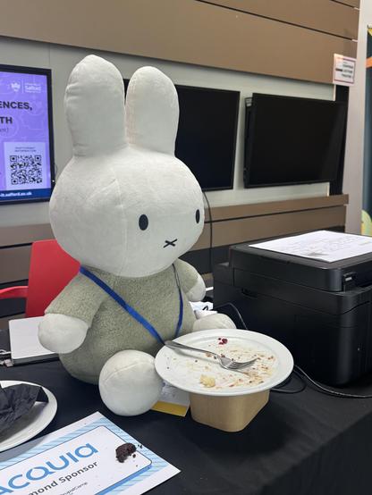 The DrupalCon Europe mascot Miffy, a stuffed rabbit, sat on a desk with an empty plate of food in front of her. 