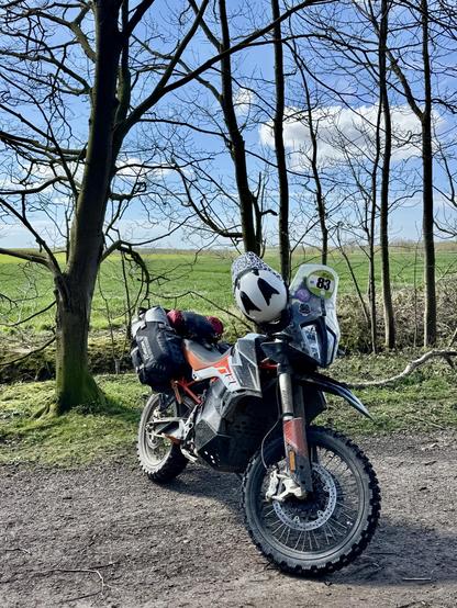 KTM motorcycle parked on a dirt track, with a line of trees behind and then green fields in the background. 