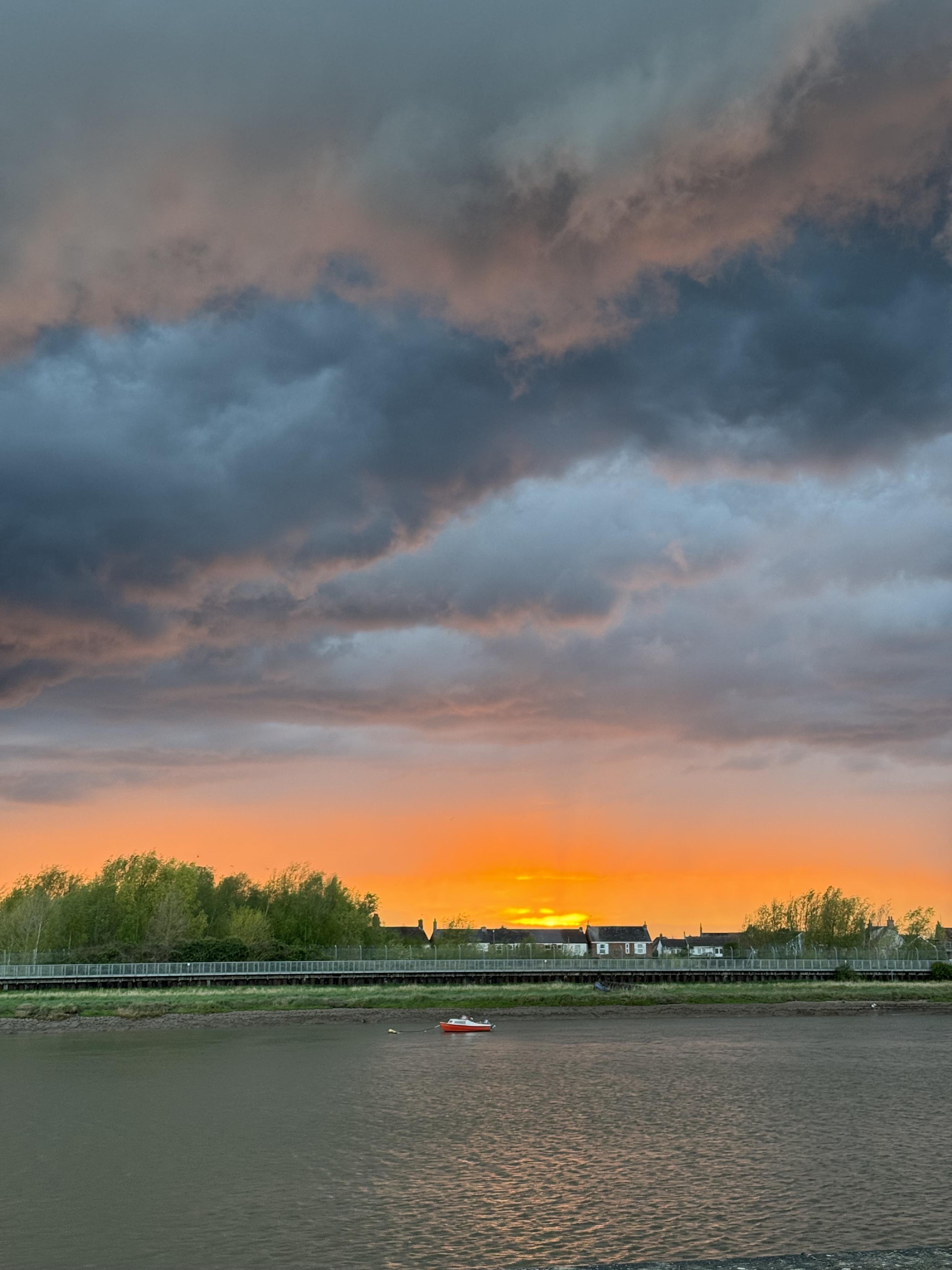 Cloudy sunset taken over a river. There’s a small red boat on the river