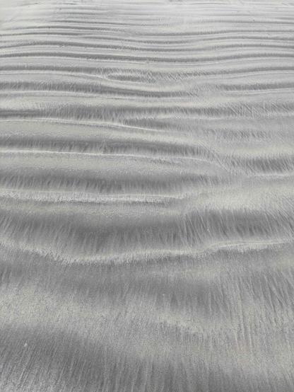 grey and silver sand on a beach giving the appearance of corrugation.