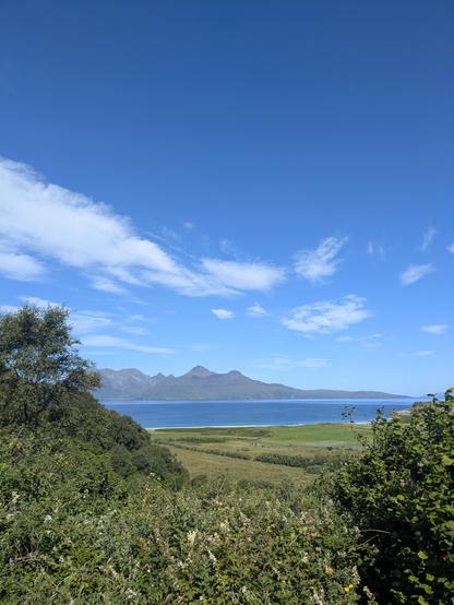 looking down across farmland to a beach and the sea on a blue sky day. island with peaks across the sea