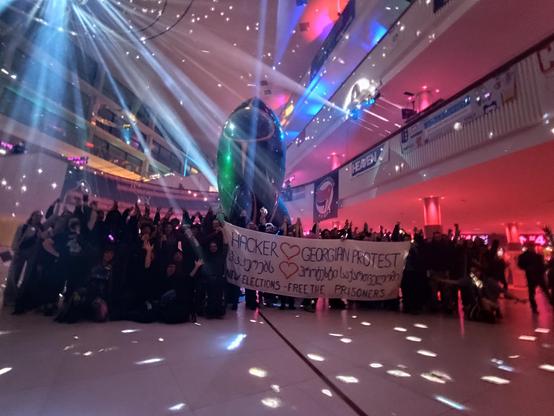 People protestesting in front of a rocket. The banner reads “Hackers love Georgian protests” and “New Elections, Free the prisoners”