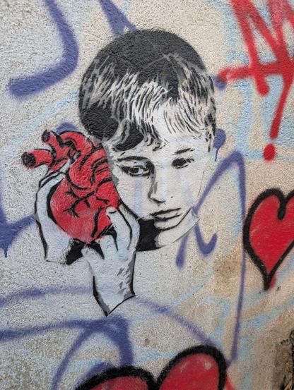 Graffiti of a young person's face holding a realistic read heart (the organ) next to their ear.