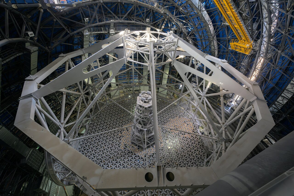 A view of the main structure of ESO’s Extremely Large Telescope from above. There is circular shape at the base with a tall metal post, joined to surrounding metal beams by five long horizontal metal supports. There is a twelve-sided metal structure at the top, with a gap in its centre, which the surrounding beams attach to.