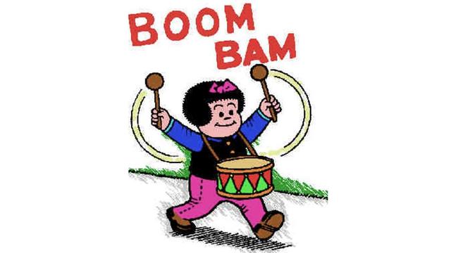 Comic illustration of Nancy marching forward cheerfully while playing a small drum strapped to her waist. She raises two wooden drumsticks in the air, with curved yellow motion lines showing her swinging motion. Red bold lettering above her reads "BOOM BAM".