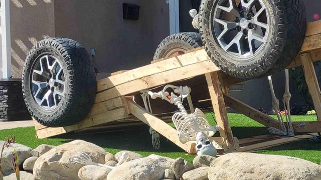 Two skeletons in a wood vehicle with real tires,a halloween display on a lawn