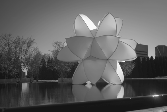 Black & white photograph of a large geometric shape sitting on a reflected in a large pool of water.