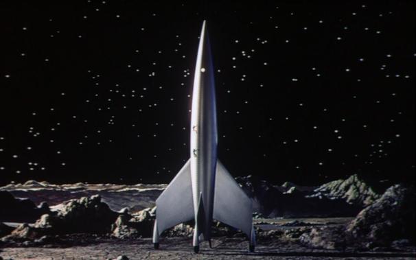 An image from the 1950 movie "Destination Moon" with a gleaming classic pointy rocket on a rocky imagined moon surface.