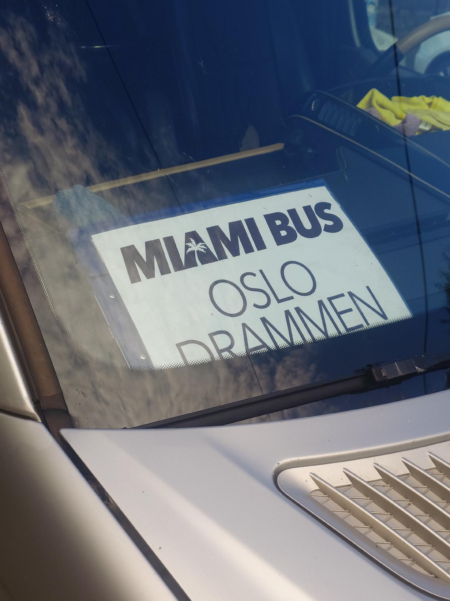 A photo of a sign in the front window of a small mini bus which reads 'Miami Bus. Oslo. Drammen.'