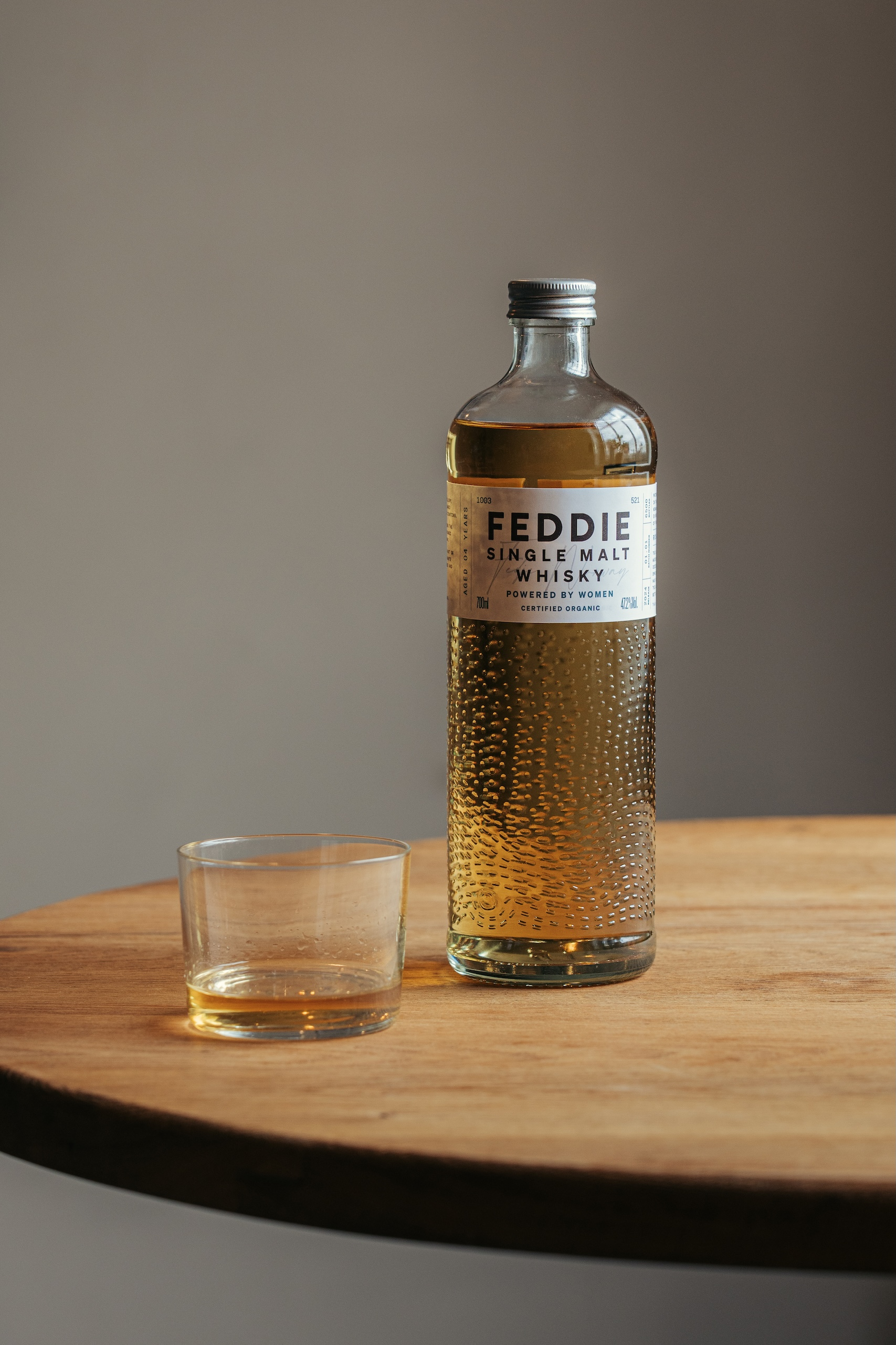 A bottle of FEDDIE signle malt whisky on a table, with a little poured into a small glass beside it.