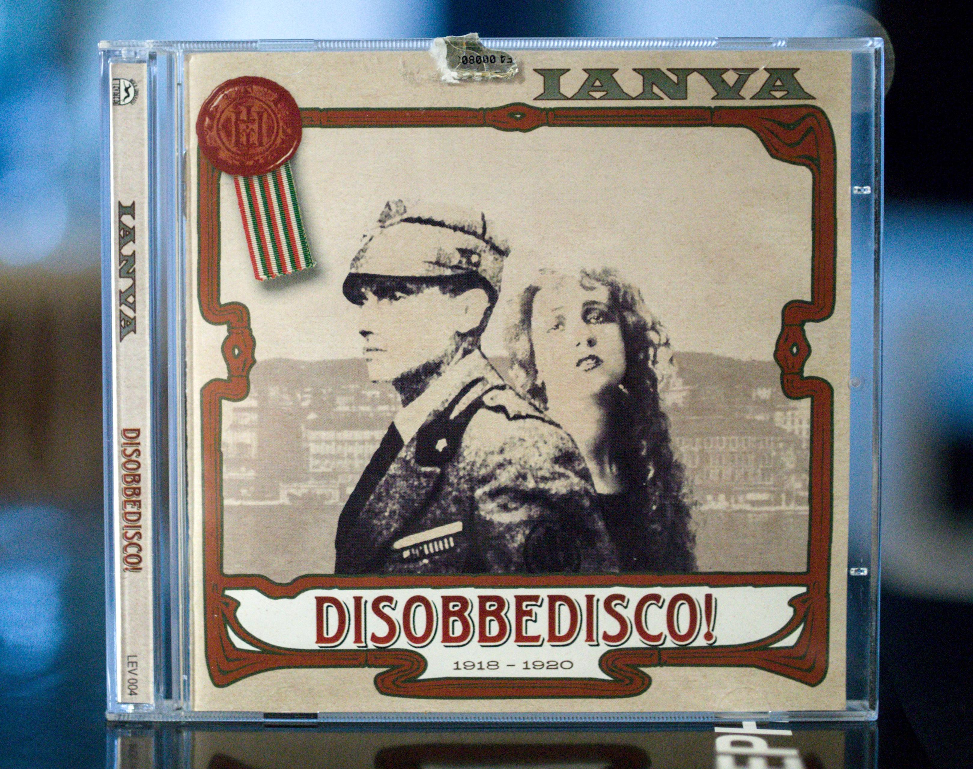 CD cover for"DISOBBEDISCO!" by IANYA, The cover art features a vintage-style illustration with a sepia-toned background. In the foreground, two figures are depicted: a man in a military-style uniform and hat, and a woman with curly hair and expressive eyes. The man is positioned to the left, facing slightly to the right, with his uniform detailed with epaulets and what appears to be a medal or badge. The woman is to the right, looking towards the viewer. Behind them, a faint, stylized cityscape is visible.