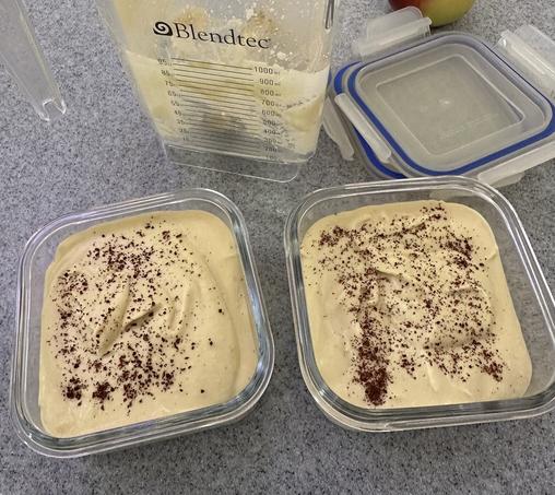 Two glass food containers full of hummus with a some deep red dried sumac dusted on top. Blender jar lurks in the background