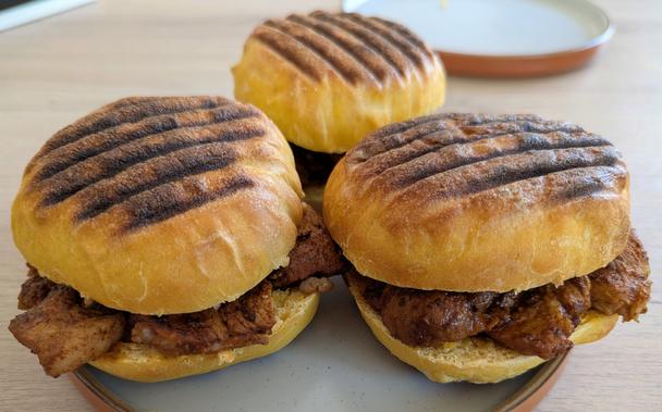 A photo of the Bifanas on a plate on a counter, from the front and showing the pieces of pork inside.