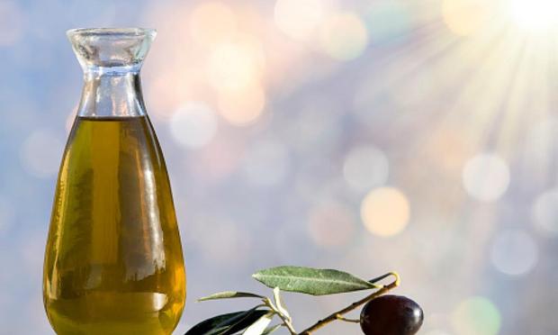 Botella de aceite de oliva y aceituna madura iluminadas por la luz del sol. (Getty Images)