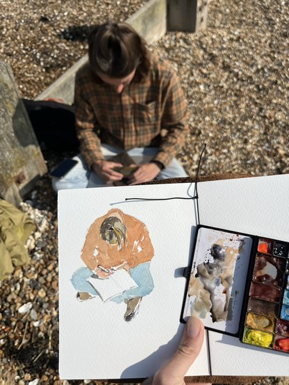 Sketch of Tolya about to start writing in his notebook and Tolya himself (sits on the sand)
