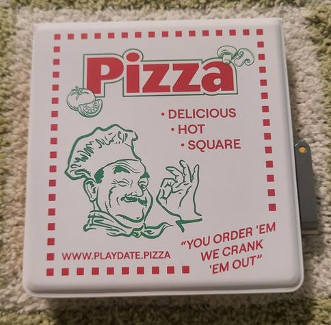 the cover for a Playdate that looks like a pizza box. it's white with a green outline of a man doing the ok symbol. in red text it says: PIZZA. DELICIOUS. HOT. SQUARE. YOU ORDER 'EM WE CRANK' EM OUT. WWW.PLAYDATE.PIZZA

there are also some outlines of veggies