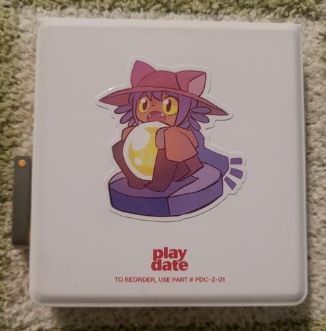 backside of the Playdate cover. has the playdate title at the bottom and centered is a sticker of Niko from Oneshot. they are riding a roomba, look excited to chomp something, and holds a large light bulb with both hands