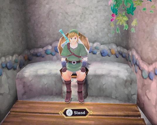 Link from the video game Skyward Sword, sitting on a toilet. There is a label below telling the player that one may press A to stand.