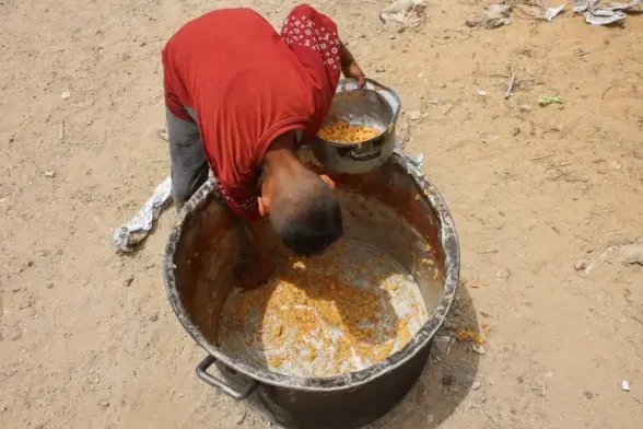 A Palestinian boy scrapes out leftovers from the bottom of a pot.