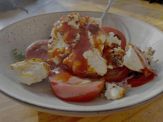 A plate of food. All jumbled up and topped with ketchup. You can see a slice of tomato in there. Vague white blobs and a green bit or two.