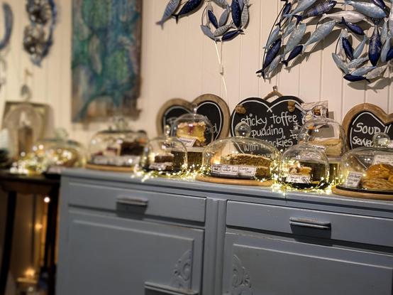 Colour photograph of a blue painted cabinet, topped with sparkling fairy lights and a selection of cakes under domed covers.