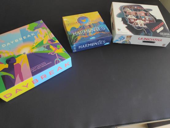 Fotografía de 3 juegos de mesa sobre una mesa con un tapete negro. De izquierda a derecha están:

Daybreak
Harmonies
La iniciativa