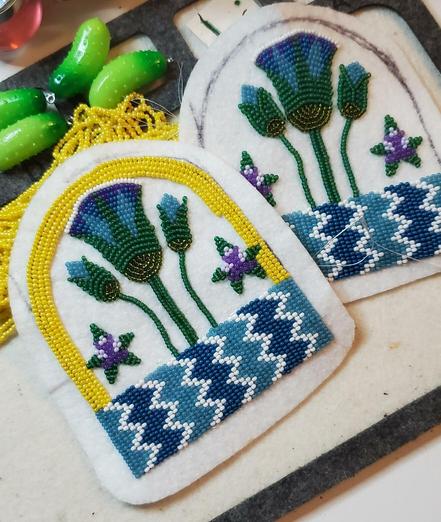 two in-progress beading projects by kiamichi of an Egyptian design made with seed beads. the color scheme is teal, blue, white, green, and purple with yellow on top/in the background. it depicts an Egyptian lotus coming out of the Nile with some decorative blooming stars next to it.