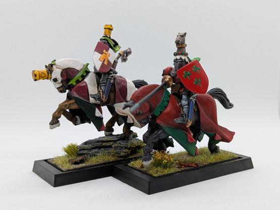 Frente a un fondo blanco, dos miniaturas de dos caballeros medievales a lomos de sendos caballos con barda, el primero con una heráldica cuarteada blanca y roja (perdón, argente y gules) y el segundo con una heráldica toda roja (campo de gules) y tres flores verdes de blasón.