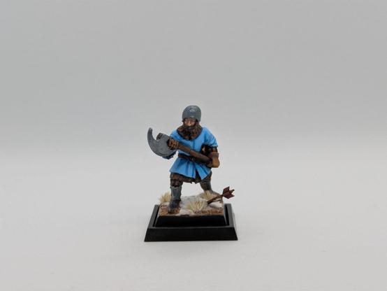 Frente a fondo blanco, un hombre de armas medieval, estilo guerra de los cien años, con un hacha a dos manos y uniforme azul claro, sobre terreno nevado