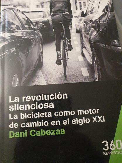 portada del libro "La revolución silenciosa. La bicicleta como motor del cambio en el siglo XXI. Dani Cabezas". Se ve una foto en blanco y negro de un ciclista circulando entre coches atascados.