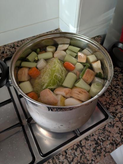 Una olla grande puesta al fuego con un montón de verduras troceadas dentro.q